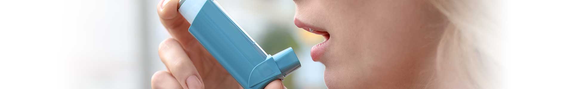 Woman's face from the side holding a blue COPD inhaler with her right hand towards her mouth